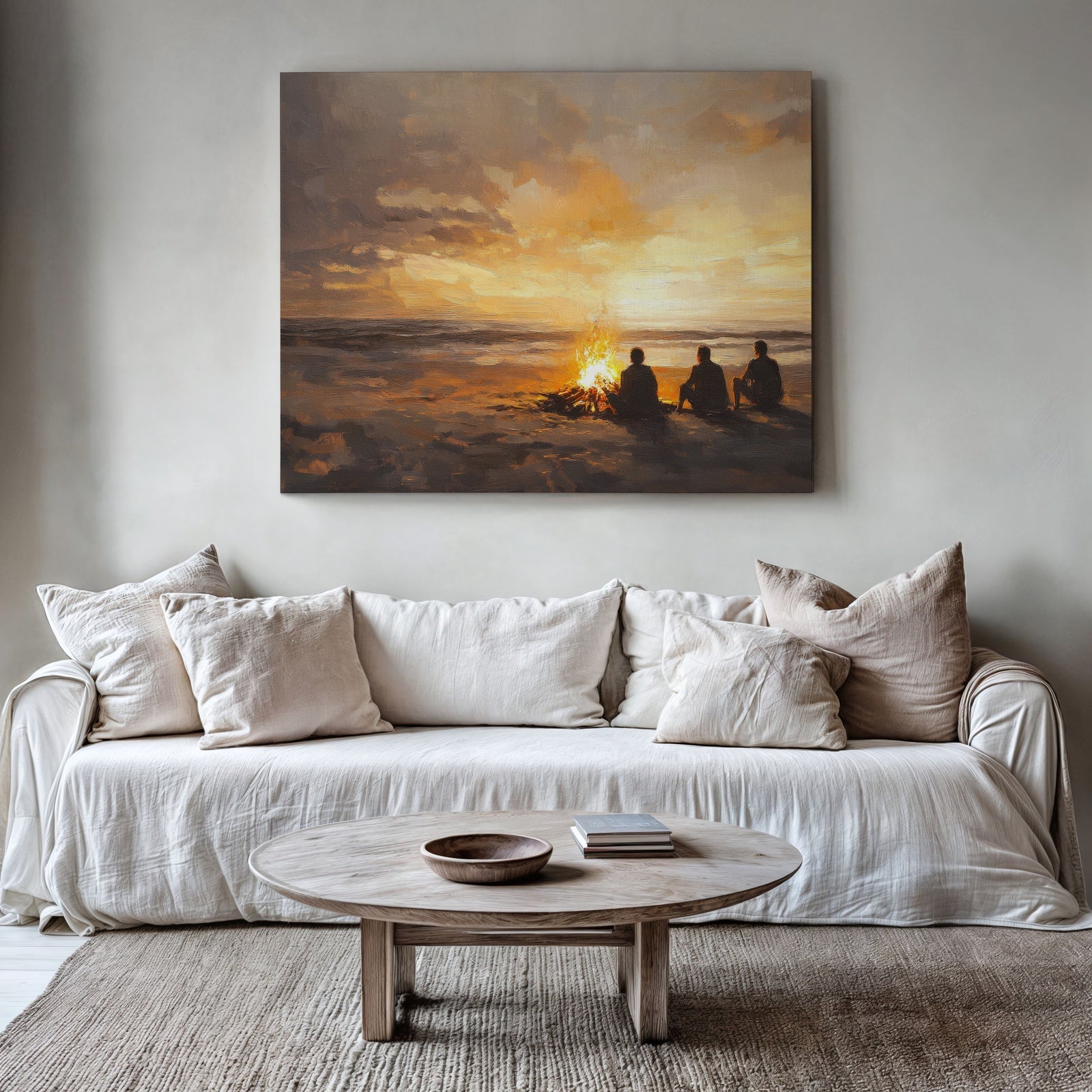 Coastal printable wall art featuring a warm sunset beach scene with three people sitting around a glowing bonfire, displayed above a neutral modern sofa with soft textures and natural decor